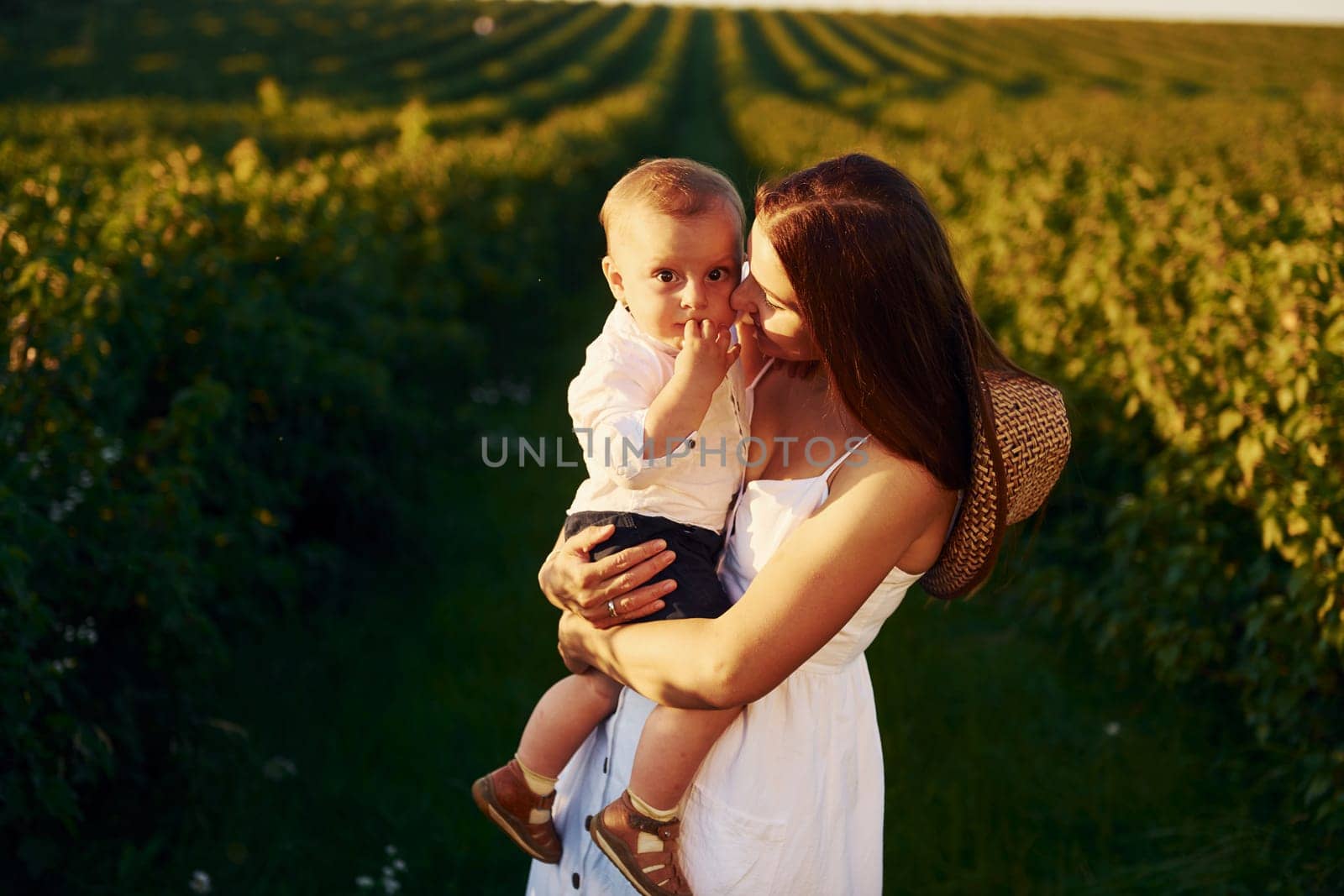 Positive mother with her son spending free time on the field at sunny day time of summer.