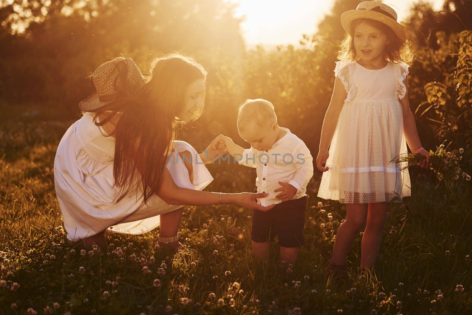 Cheerful family of mother, little son and daughter spending free time on the field at sunny day time of summer.