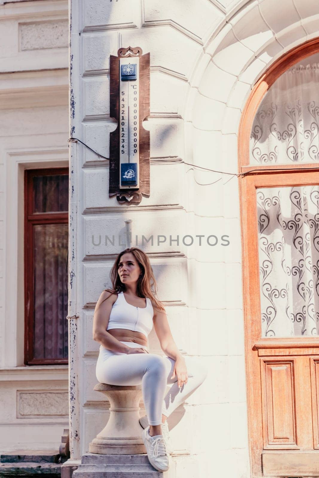 Woman wall sits. A brunette woman in a white suit sits near an old antique door on a sunny day.