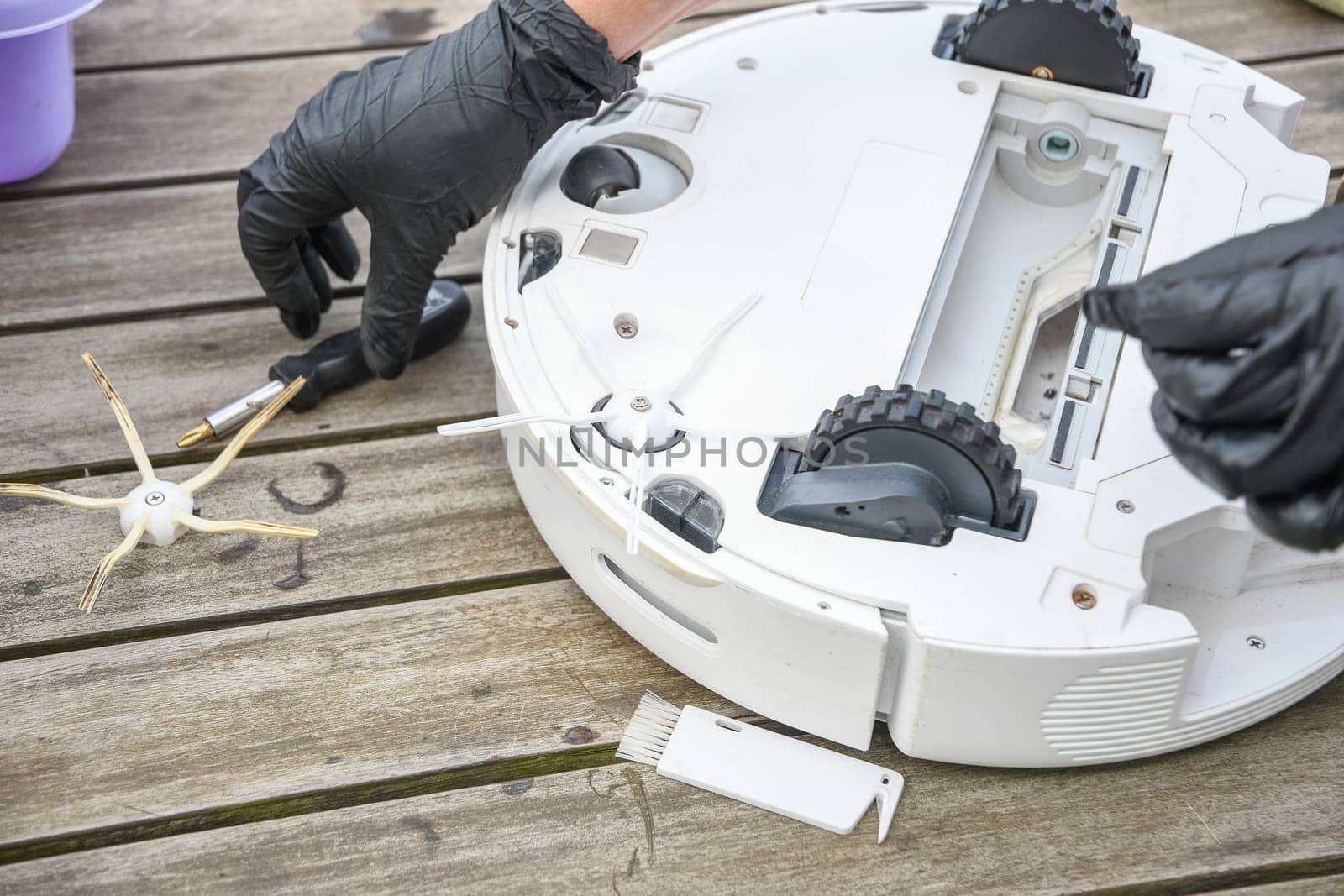 a woman unscrews the side brush from a robot vacuum cleaner with a screwdriver, routine maintenance of equipment for long-term use, high quality photo