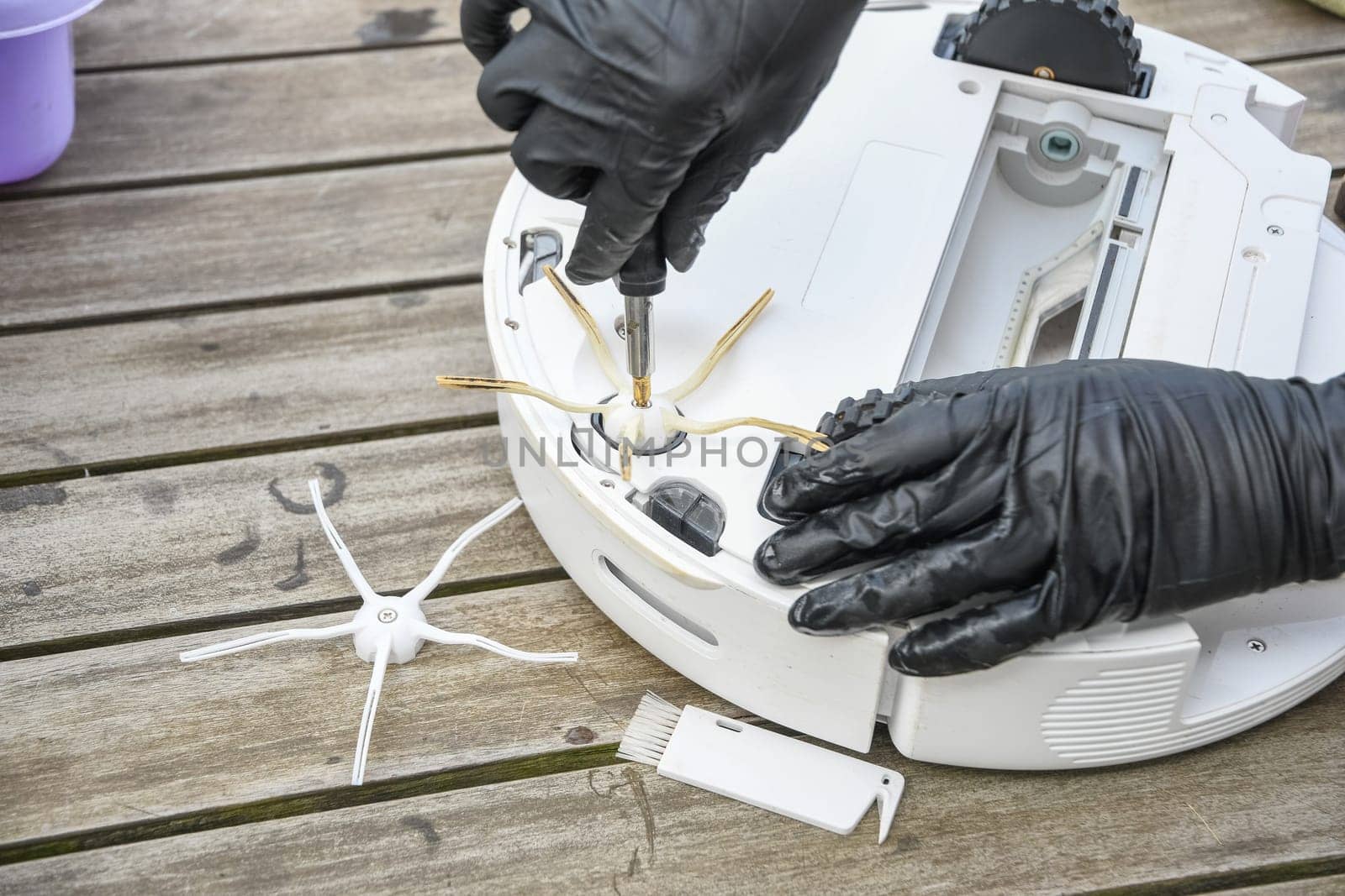 a woman unscrews the side brush from a robot vacuum cleaner with a screwdriver, routine maintenance of equipment for long-term use, high quality photo