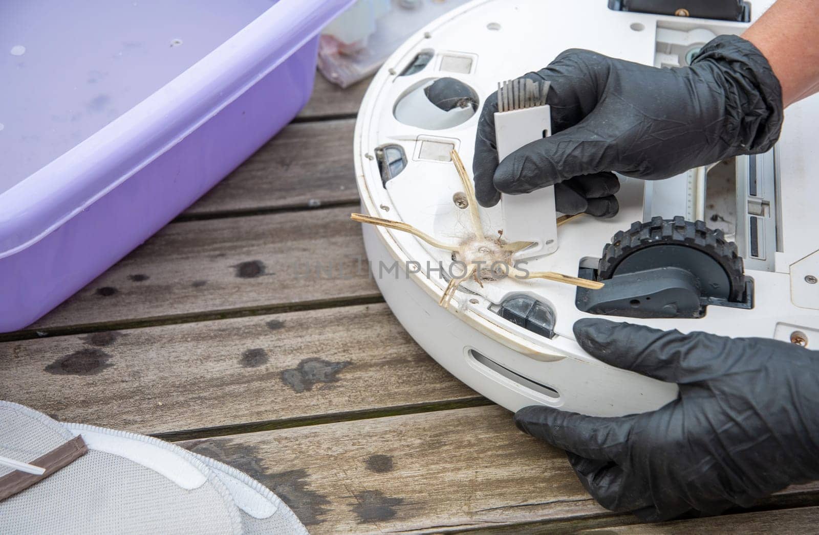a woman cuts tangled hair with a knife on a brush with three side processes at a vacuum cleaner robot, routine maintenance of equipment for long-term use, high quality photo