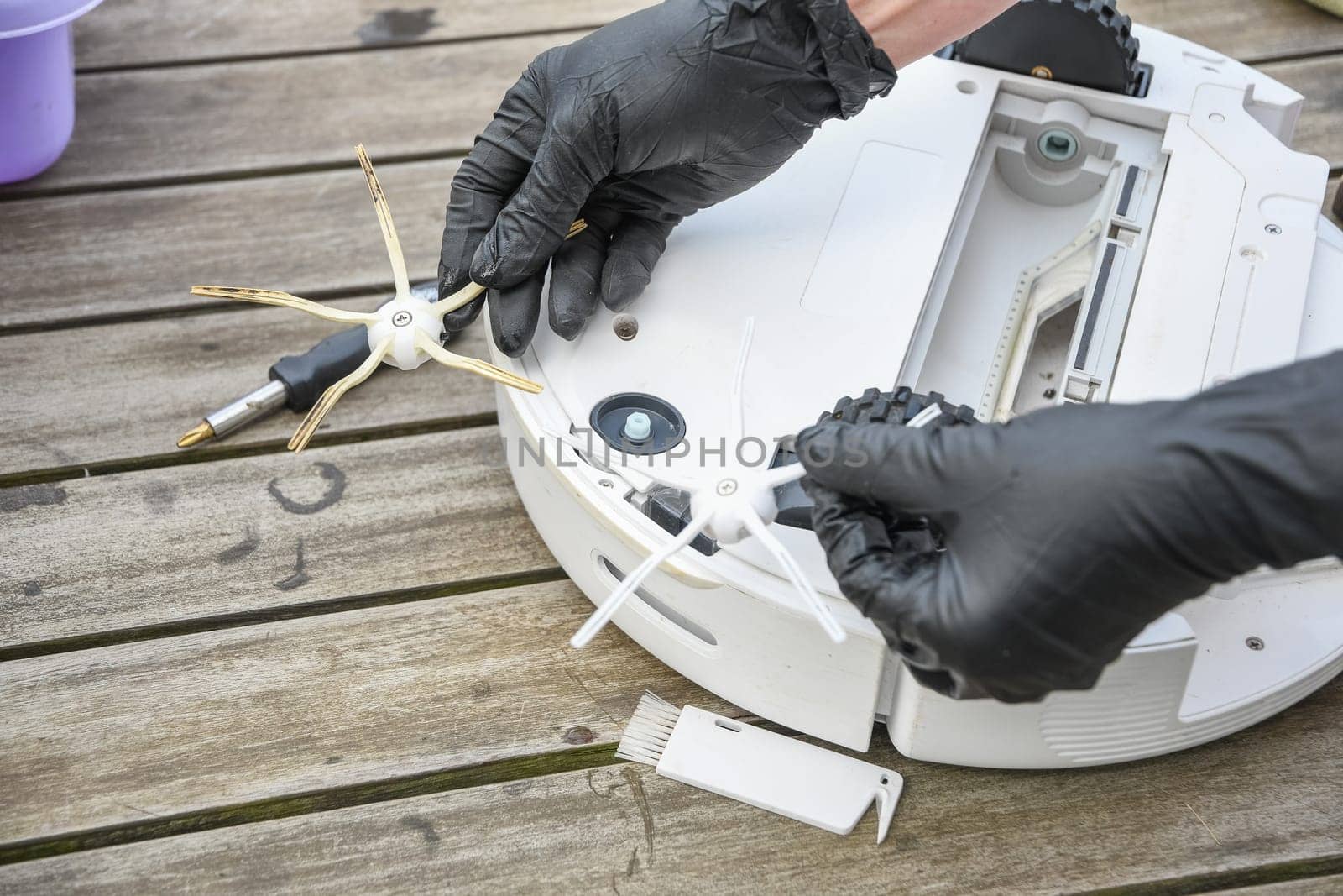 a woman unscrews the side brush from a robot vacuum cleaner with a screwdriver, routine maintenance of equipment for long-term use, high quality photo