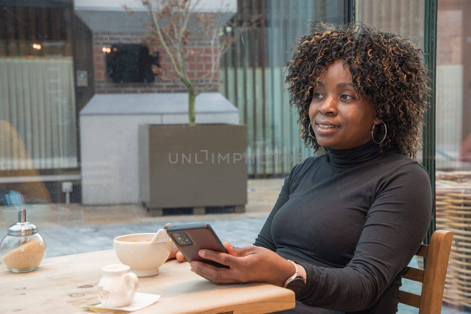 young african american woman sitting in a cafe with a cup of hot coffee, watching a social media feed in a smartphone, using technology, high quality photo, High quality photo