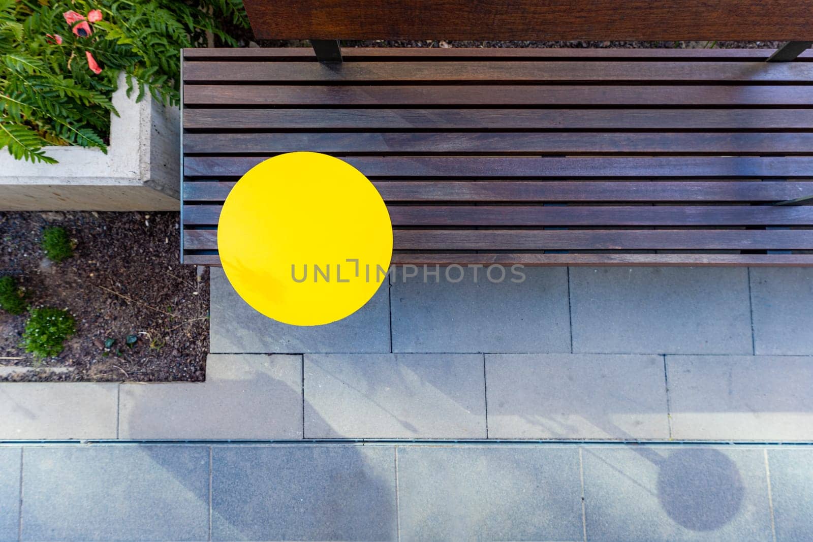 Top view of a wooden bench with a round yellow table in the garden