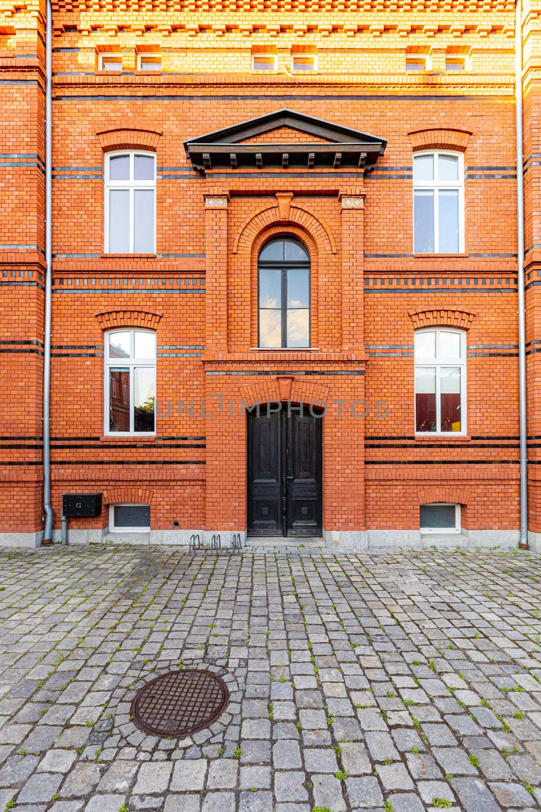 The front of a renovated tall brick building with large black doors by Wierzchu