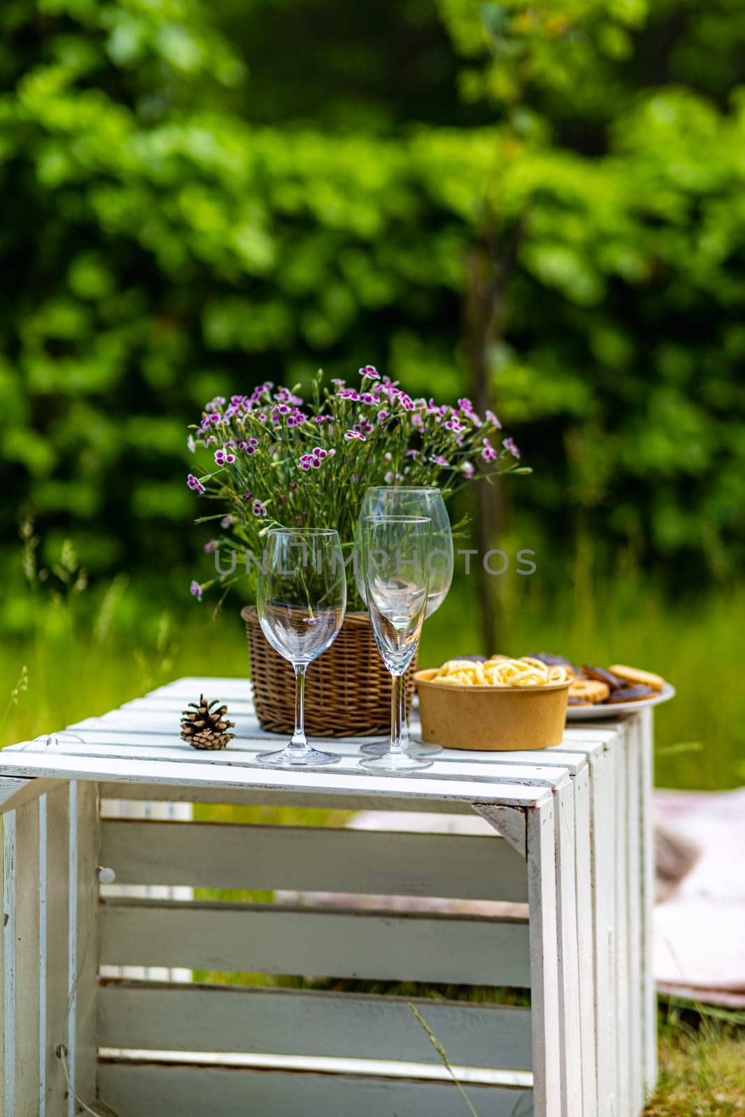 A green garden with a white wooden crate on which there are glasses, flowers and snacks in bowls