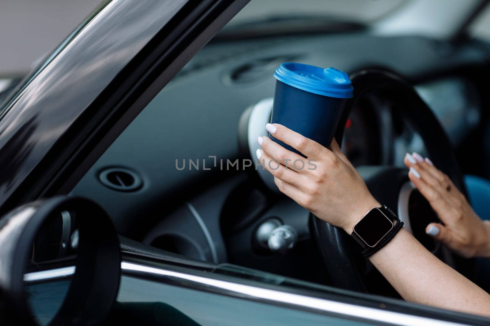 cropped photo of woman's hand holding blue paper cup of coffee in car. Hot drink take away. Travel with coffee. Concept of coffee with you. Mockup.