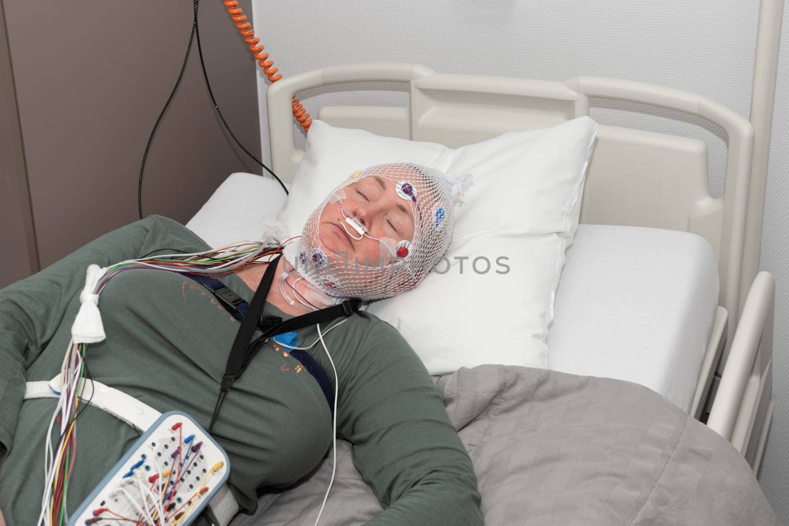 Middle aged woman measuring brain waves, examining polysomnography in sleep laboratory, High quality photo