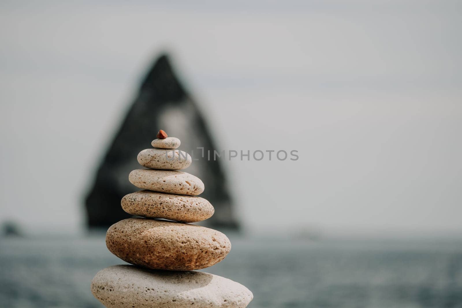 Pyramid stones on the seashore with warm sunset on the sea background. Happy holidays. Pebble beach, calm sea, travel destination. Concept of happy vacation on the sea, meditation, spa, calmness.