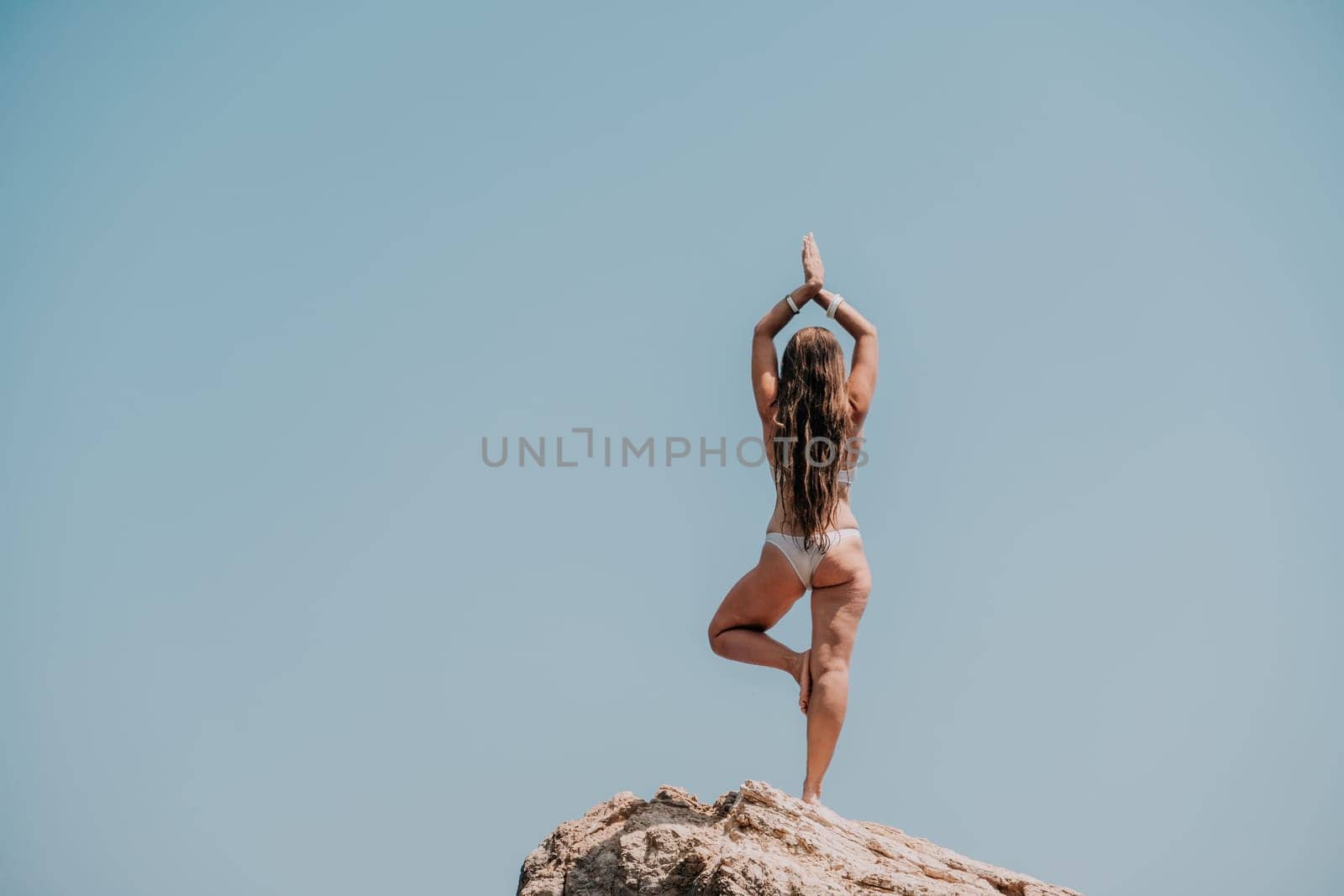 Woman meditating in yoga pose silhouette at the ocean, beach and rock mountains. Motivation and inspirational fit and exercising. Healthy lifestyle outdoors in nature, fitness concept.