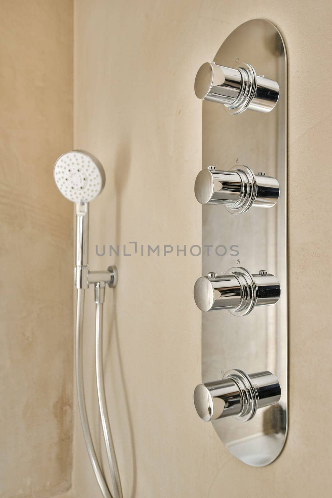 a wall mounted shower with two handsets and an overhead hand showerhead in the background is a tan colored wall