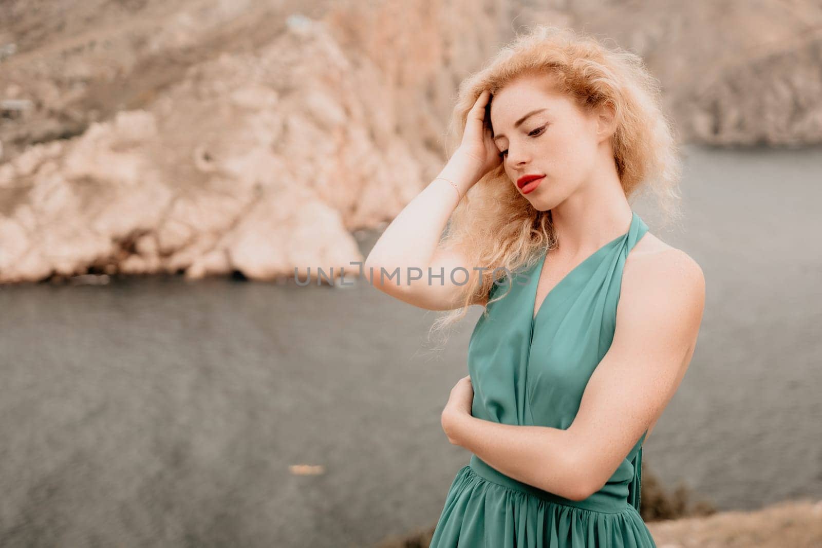 Side view a Young beautiful sensual woman in a mint long dress posing on a volcanic rock high above the sea during sunset. Girl on the nature on overcast sky background. Fashion photo