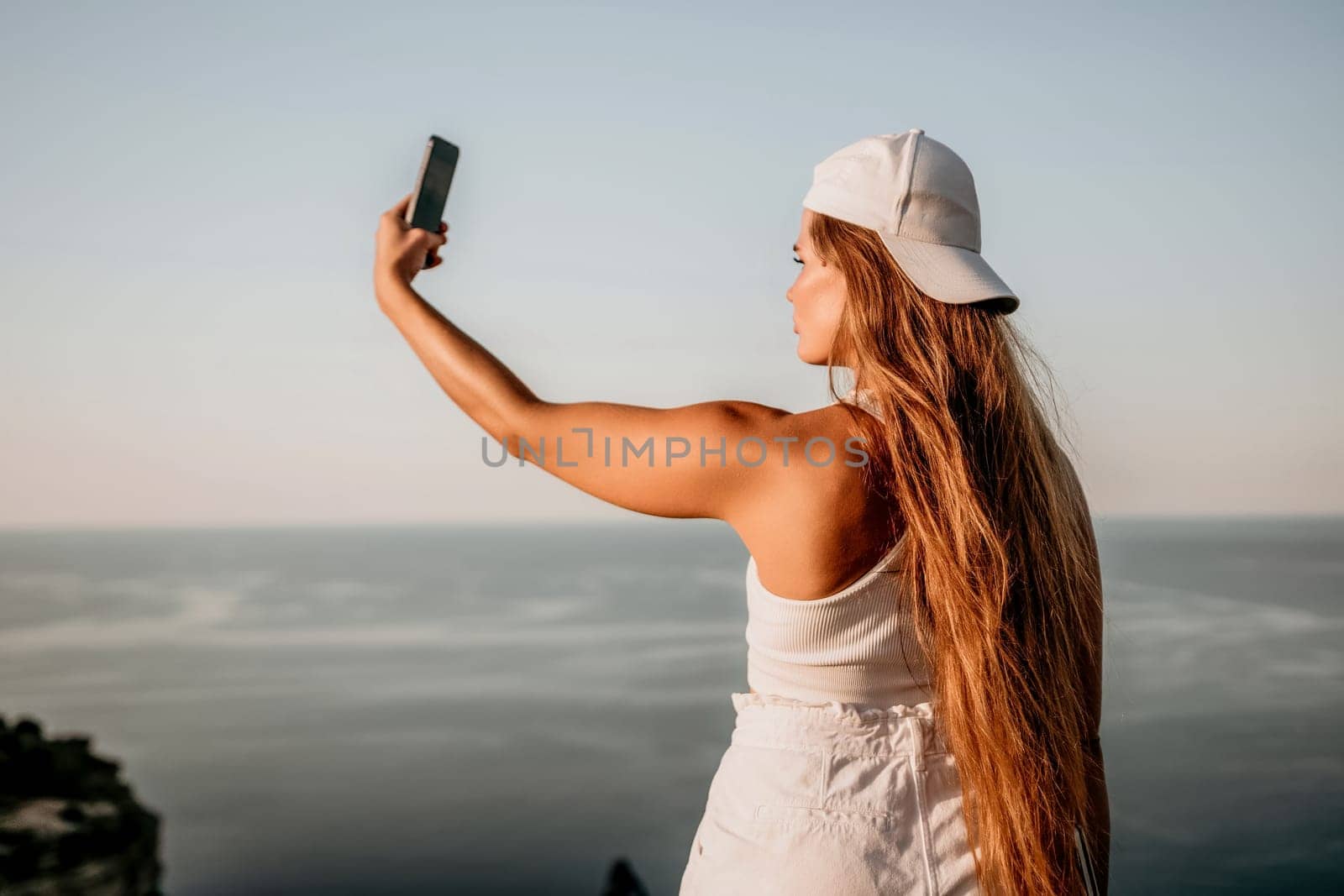 Woman travel sea. Happy tourist in hat enjoy taking picture outdoors for memories. Woman traveler posing on the beach at sea surrounded by volcanic mountains, sharing travel adventure journey by panophotograph