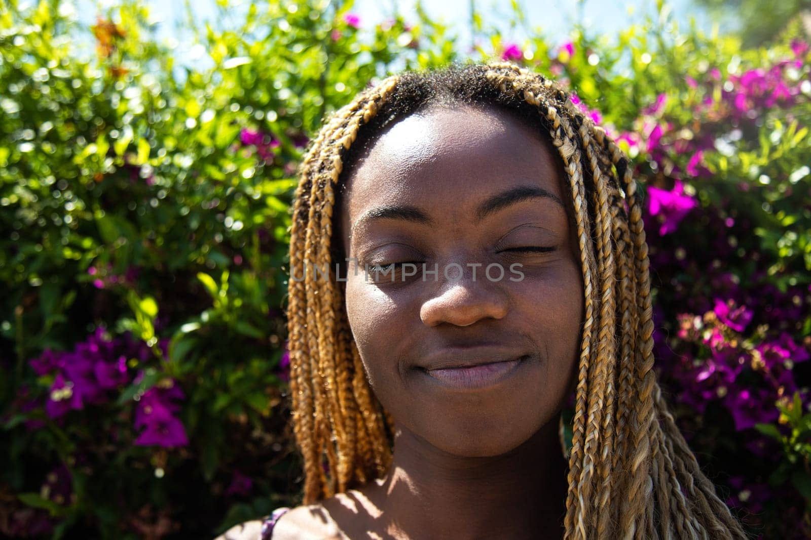 Headshot of african american young woman with eyes closed surrounded by greenery and flowers. Nature.