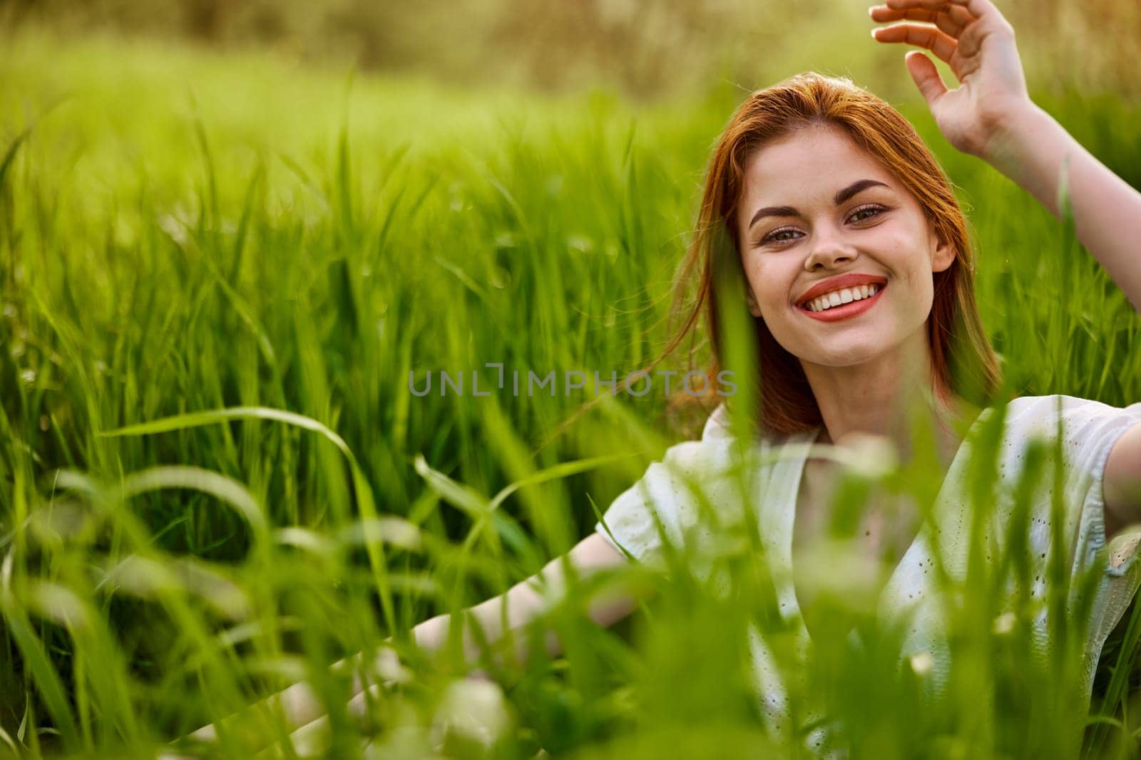 cheerful woman sitting in grass looking at camera smiling at camera by Vichizh