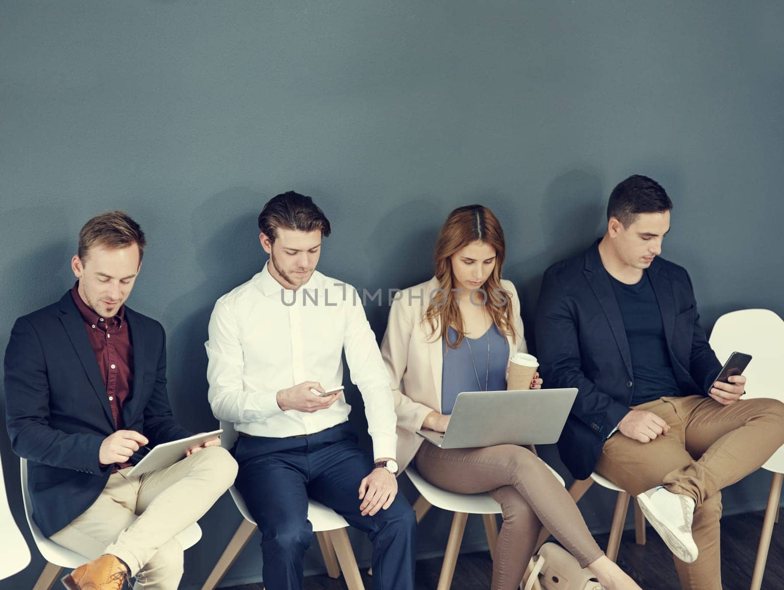 Weve been shortlisted, success is ours. a group of businesspeople using different wireless devices while waiting in line for an interview. by YuriArcurs