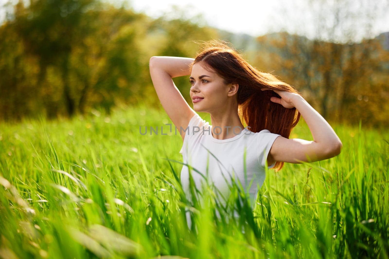 beautiful woman sitting in tall grass adjusting her hair by Vichizh