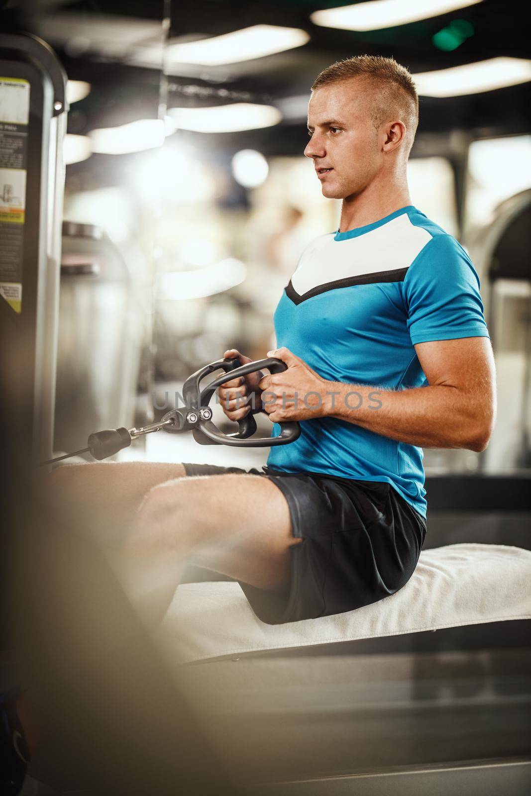 Shot of a muscular guy in sportswear working out at the hard training in the gym. He is pumping up back muscle with heavy weight.