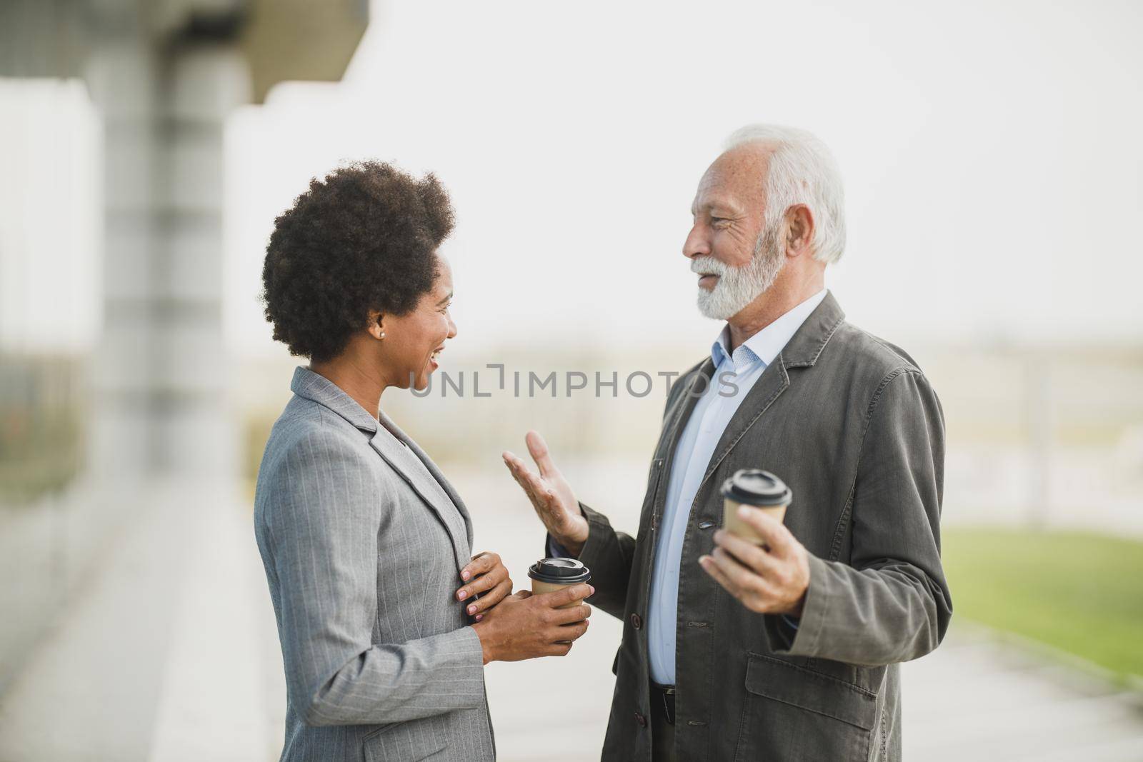 Shot of two successful multi-ethnic business people talking while having a coffee break in front of the office building.