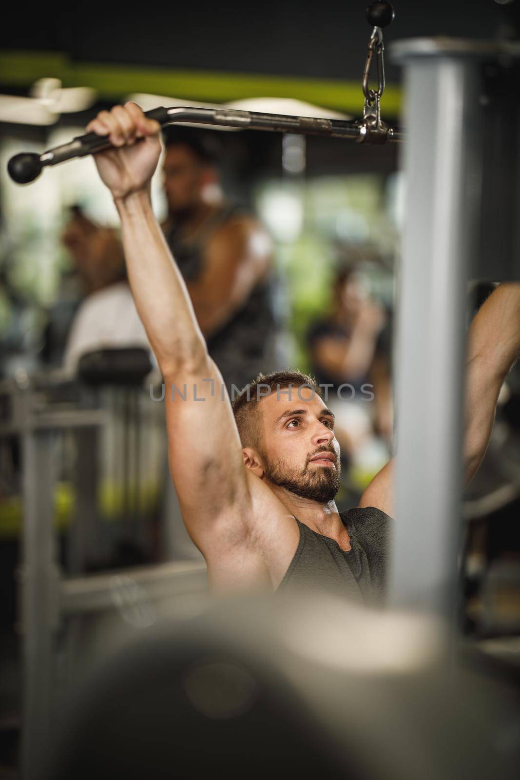 Shot of a muscular guy in sportswear working out at the gym machine. He is pumping up back muscle with heavy weight.