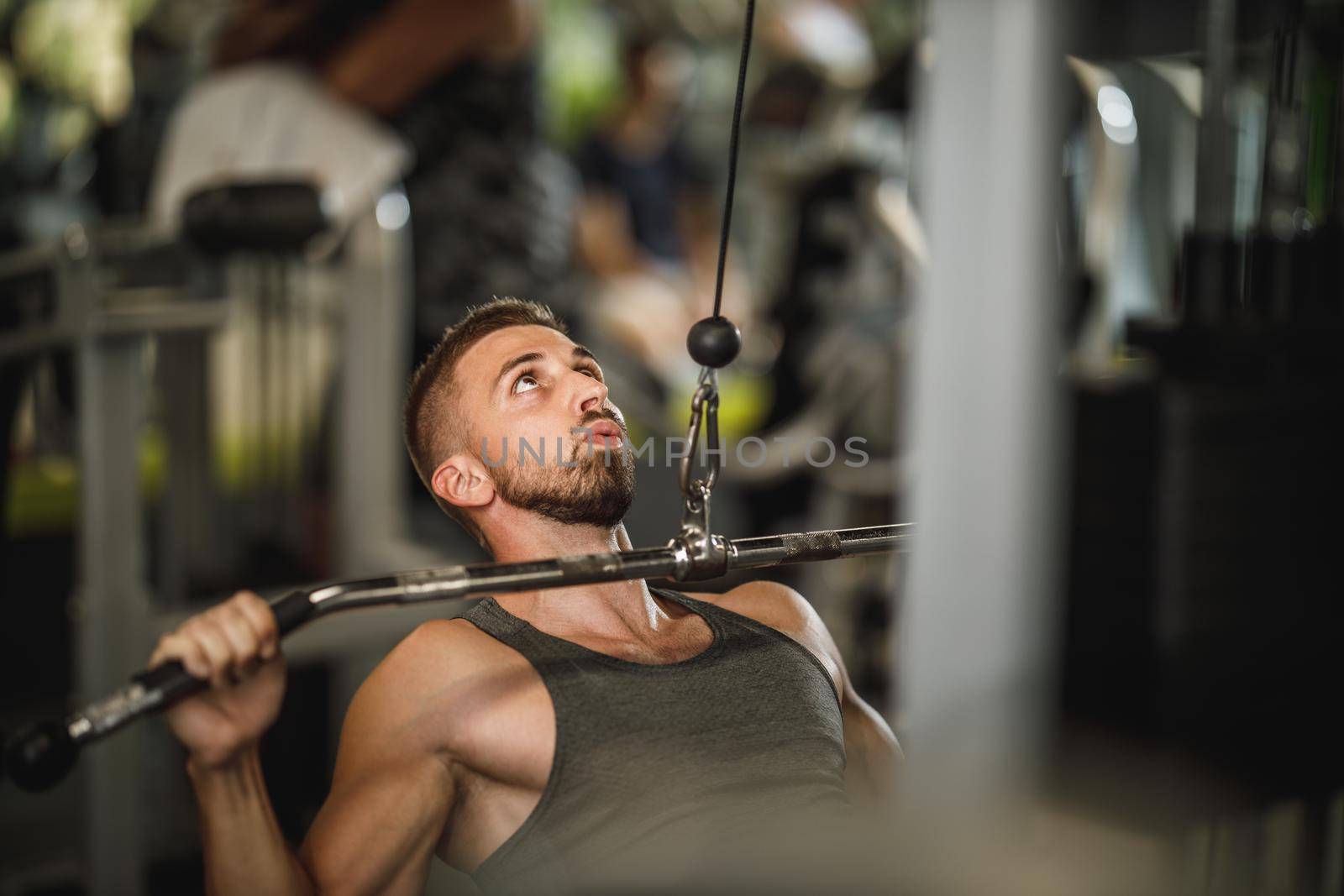 Shot of a muscular guy in sportswear working out at the gym machine. He is pumping up back muscle with heavy weight.