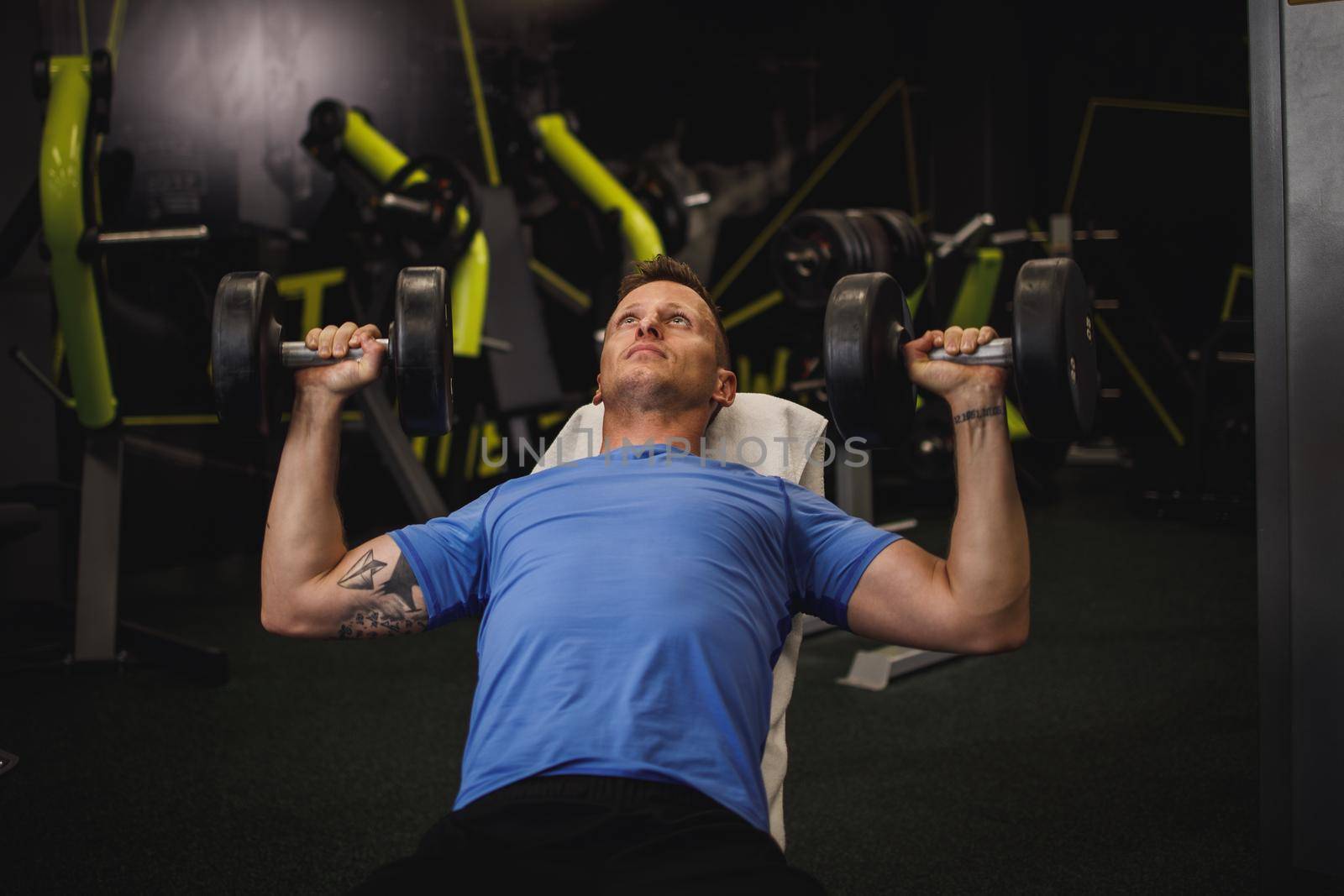 Shot of a muscular guy in sportswear working out at the hard training in the gym. He is pumping up chest muscule with heavy weight.