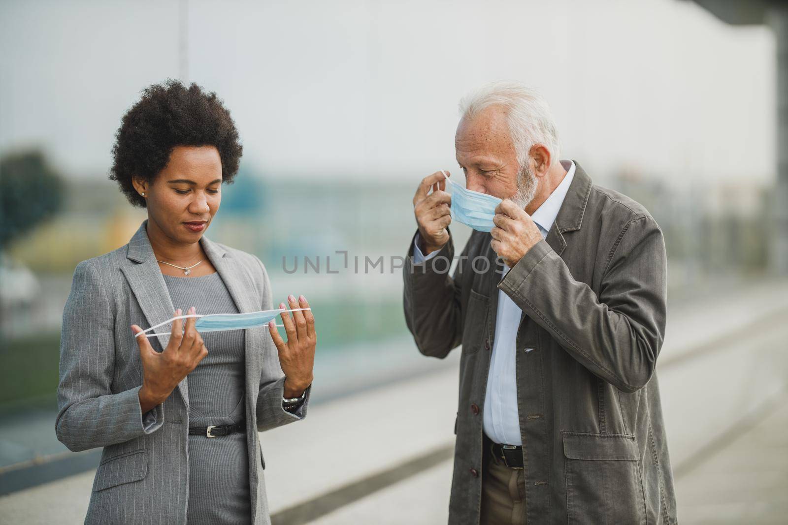 Shot of two successful multi-ethnic business people using protective mask while having a quick break in front of the office building during COVID-19 pandemic.