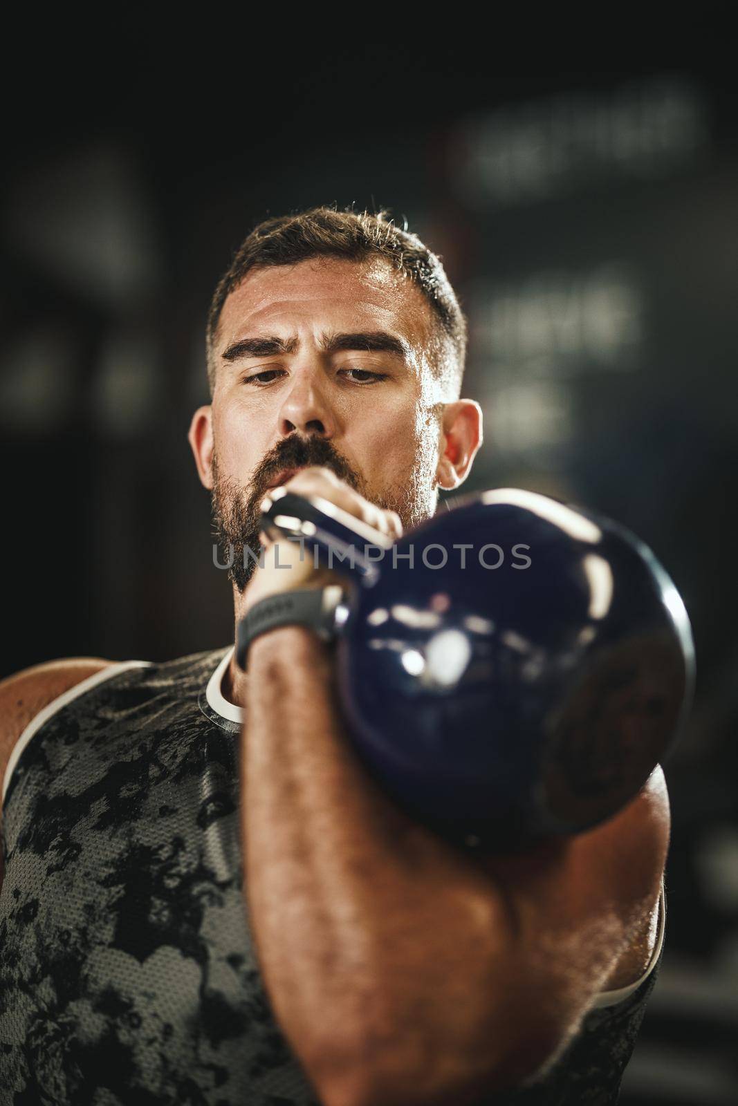 Shot of a muscular guy in sportswear doing push press exercises with kettlеbell at the gym.