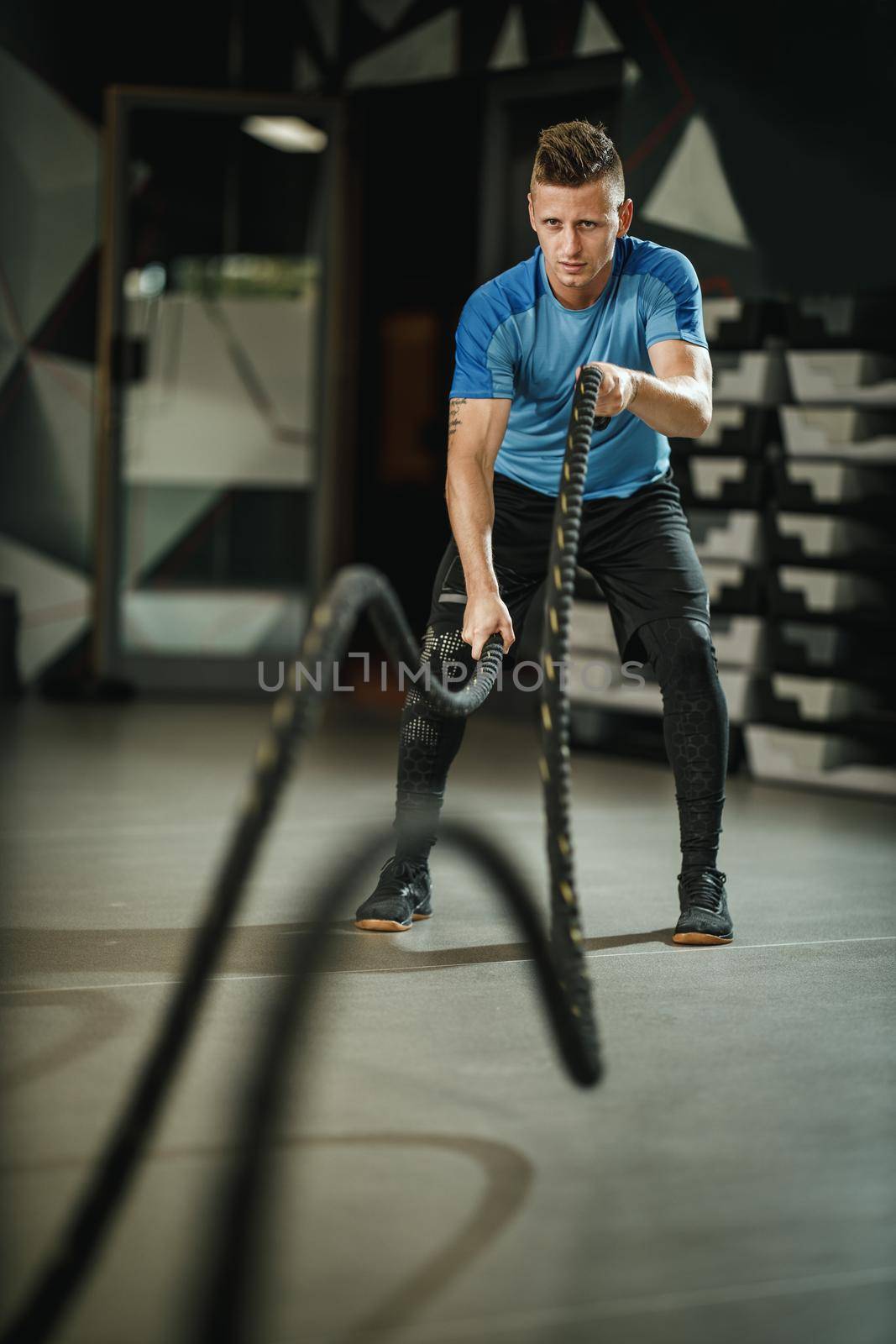 Shot of a muscular guy in sportswear doing exercises with ropes at the gym.