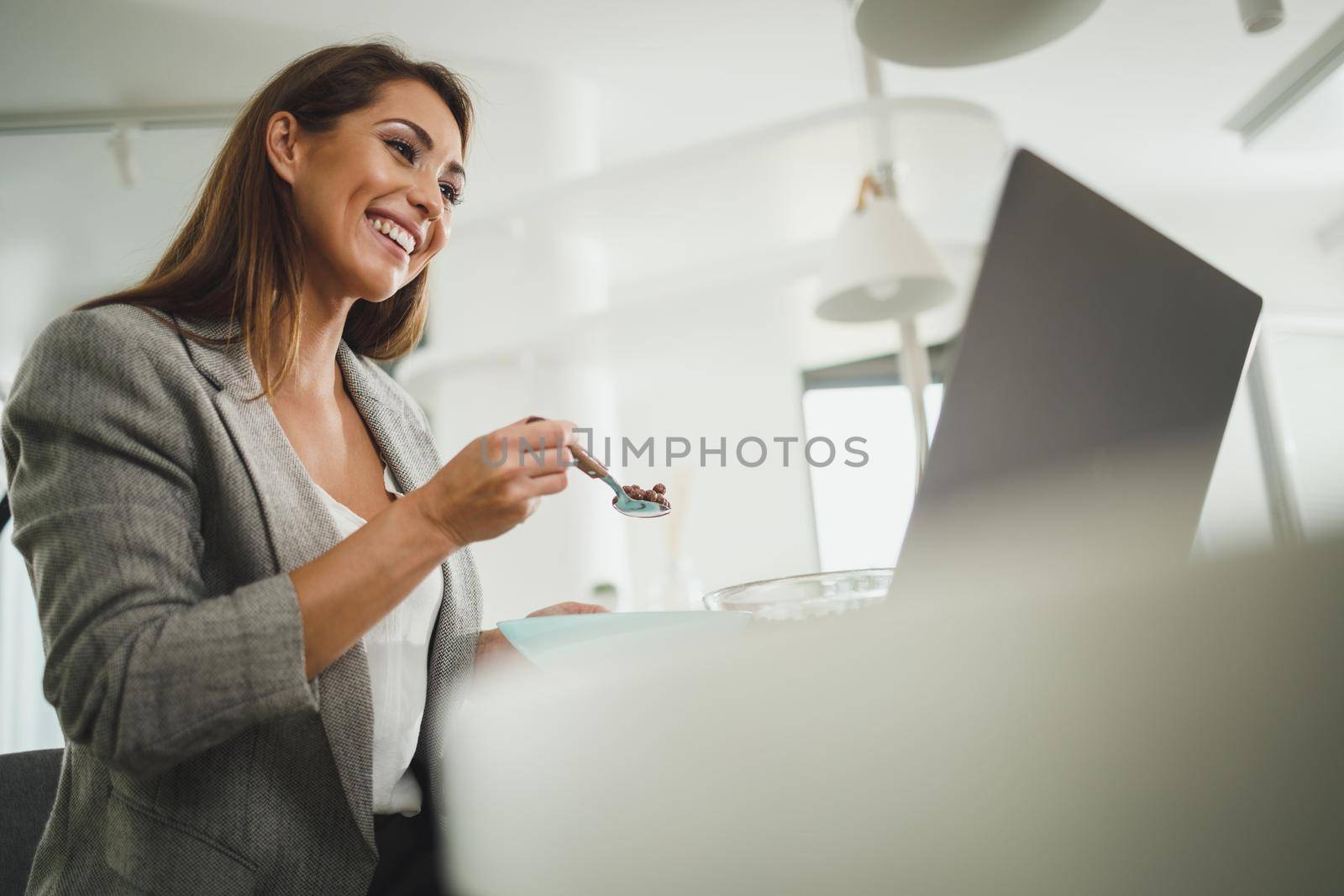 Shot of a young business woman using on her laptop while having a breakfast at home.