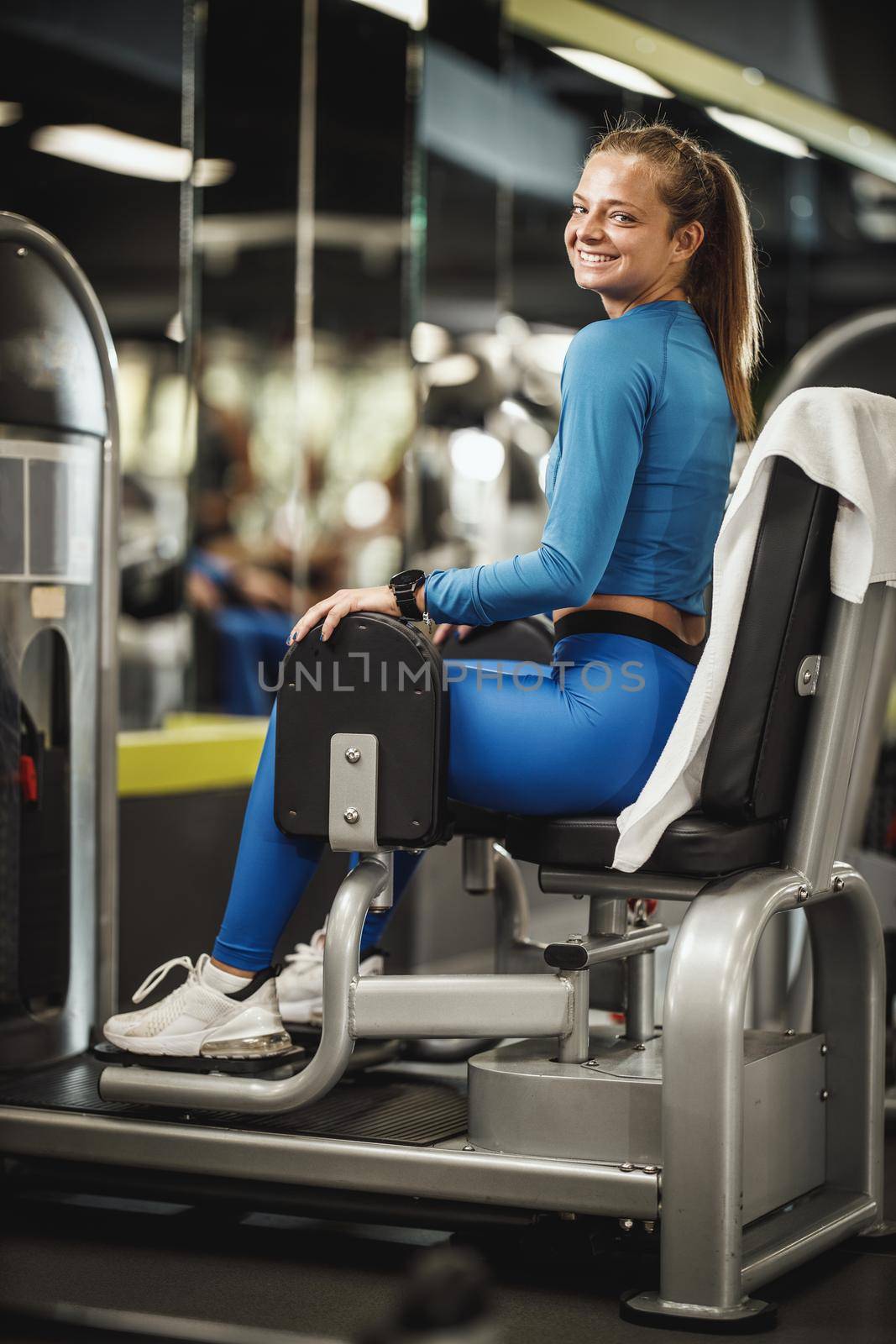 Shot of a muscular young woman in sportswear working out at the gym. She is pumping up her buttocks on machine.
