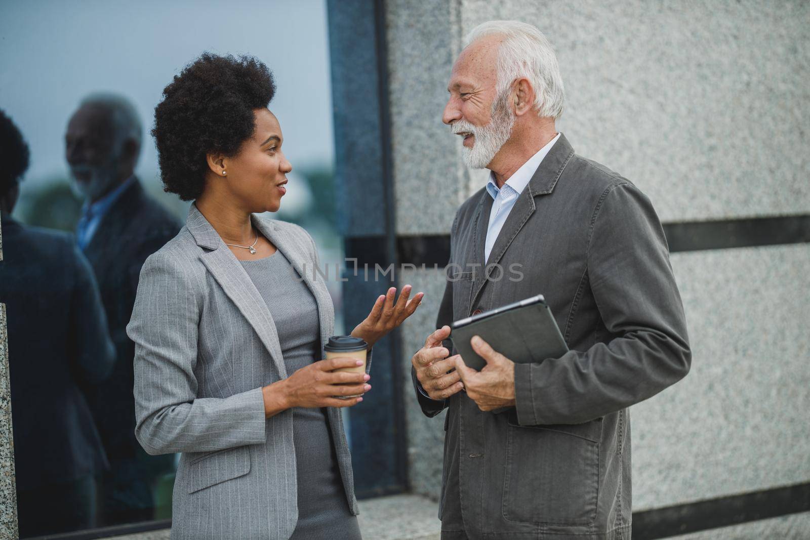 Shot of successful black businesswoman and her senior male colleague having a discussion during a coffee break in front of the office building.