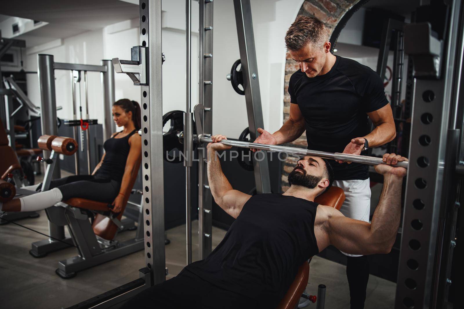 Shot of a muscular guy in sportswear working out with personal trainer at the gym. He is pumping up chest muscule during a hard ttraining.