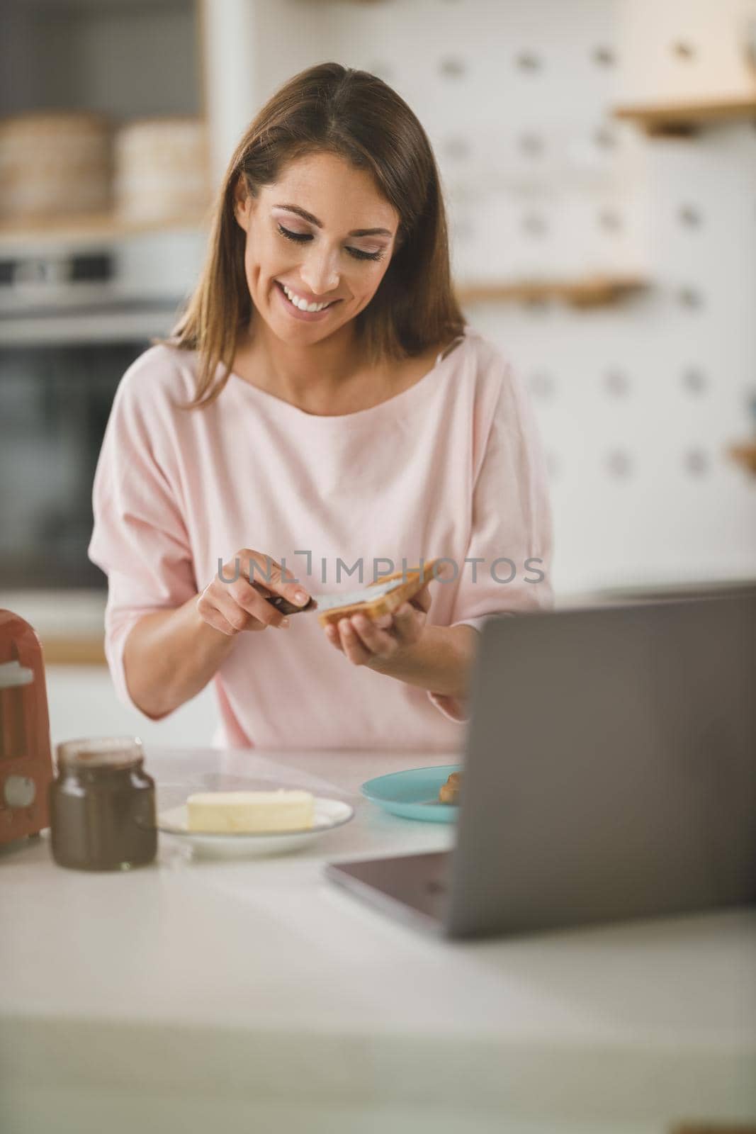 Shot of a young woman spreading butter onto toast in her kitchen.