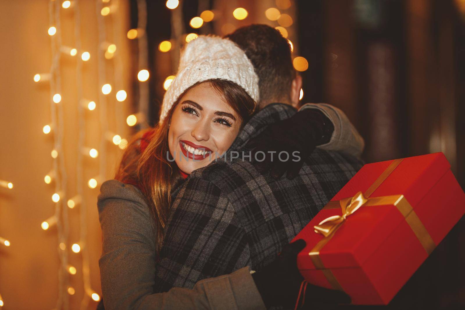 Shoot of a cheerful young couple are having fun in the city street at the Christmas night. They are hugging and giving holidays presents to each other.