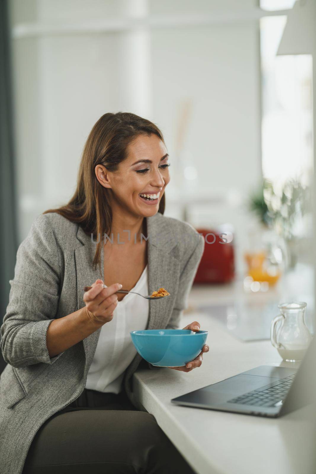 Shot of a young business woman having a breakfast while using laptop in the her kitchen during getting ready to go to work.