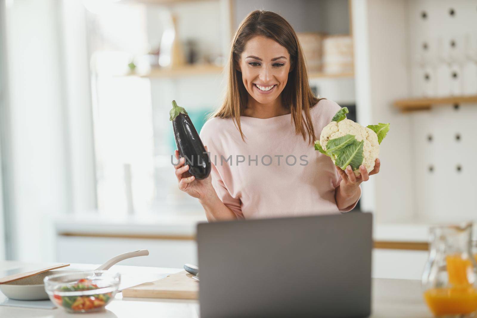 Shot of a young woman using laptop to make a vlog with someone while preparing a healthy meal at home.