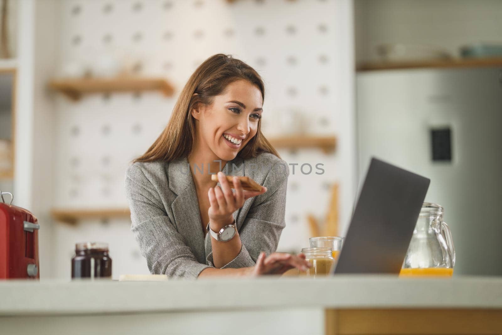 Shot of a multi-tasking young business woman surfing on social media and having a breakfast at home while getting ready to go to work.
