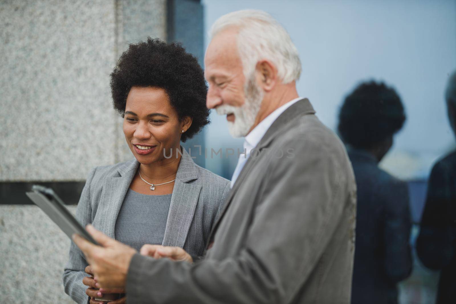 Shot of successful black businesswoman and her senior male colleague using digital tablet and having a discussion during a coffee break in front of the office building.