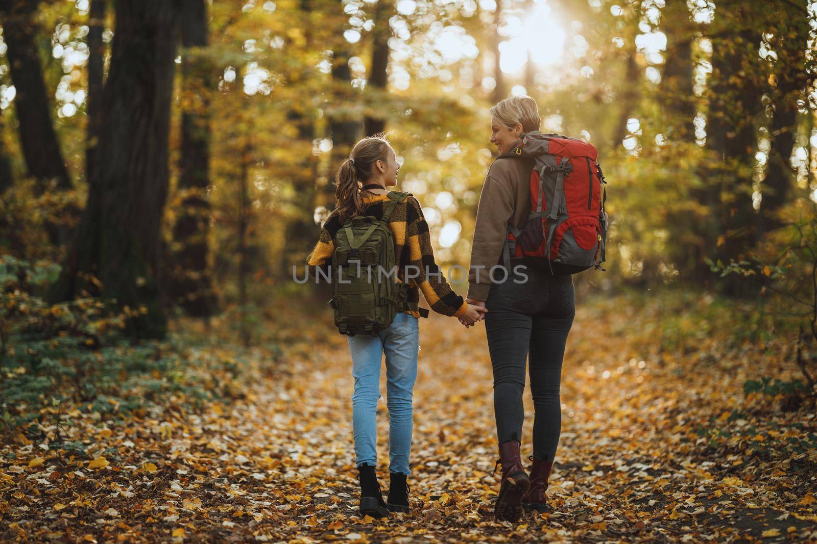 Rearview shot of a teen girl and her mom walking together through the forest in autumn.