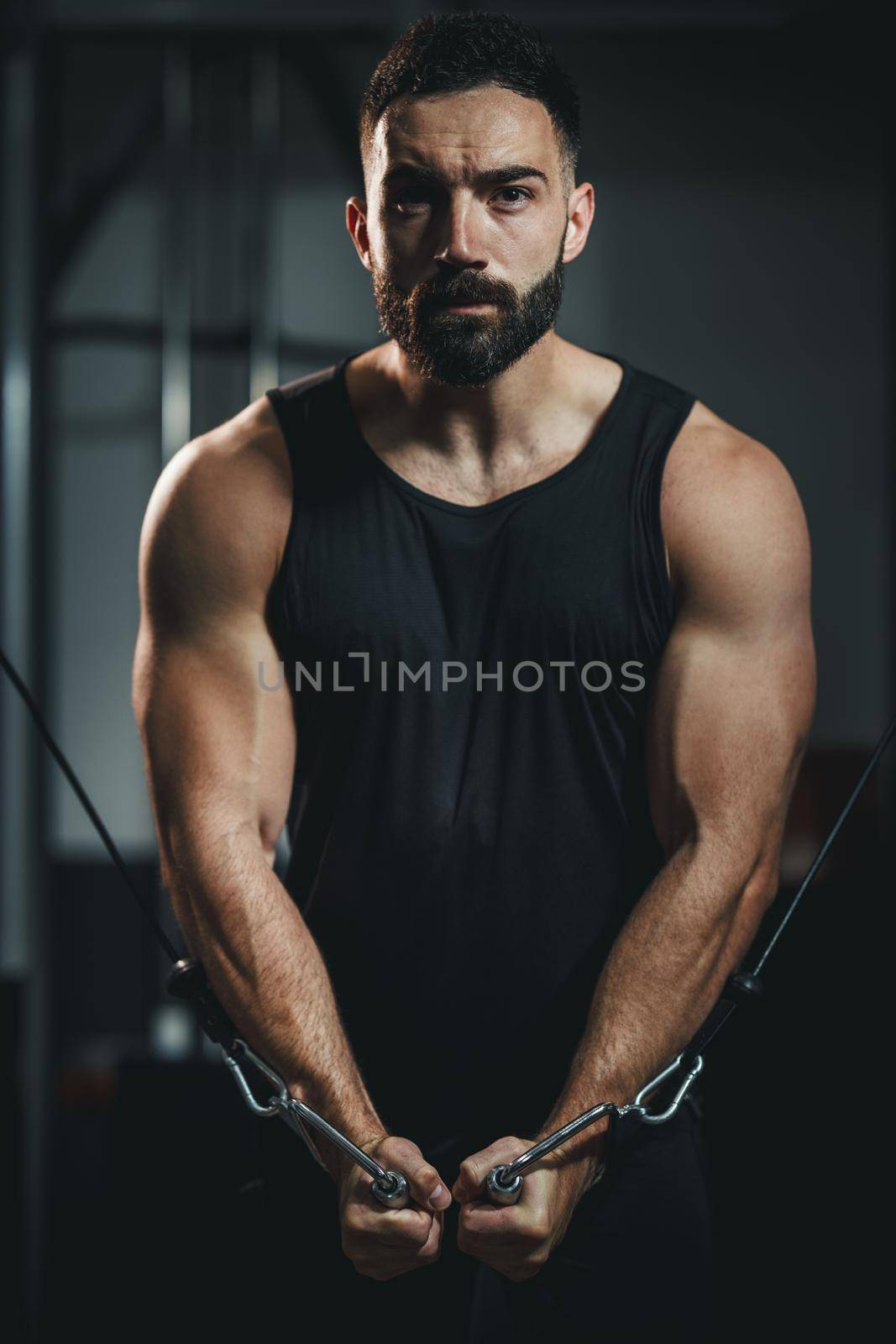 Shot of a muscular guy in sportswear working out at the gym. He is doing hard exercises for chest on cable machine during a strength training.