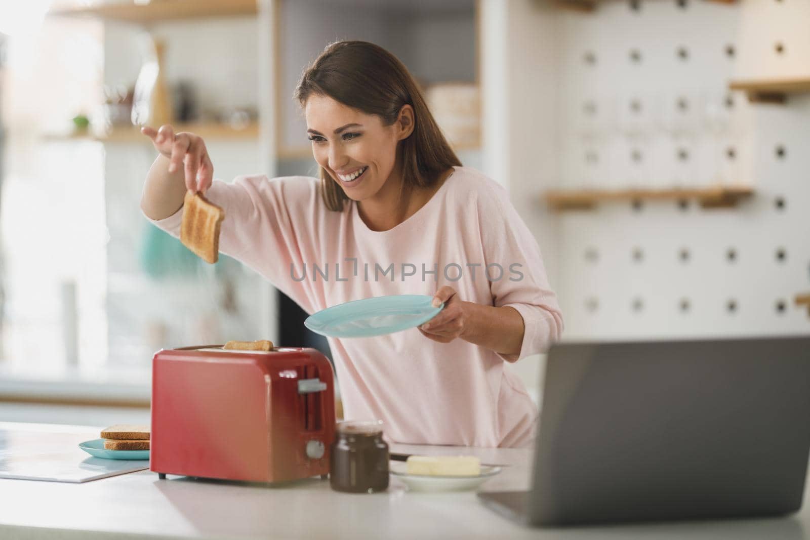 Shot of a young woman roasting a piece of toast in toaster for breakfast at home.