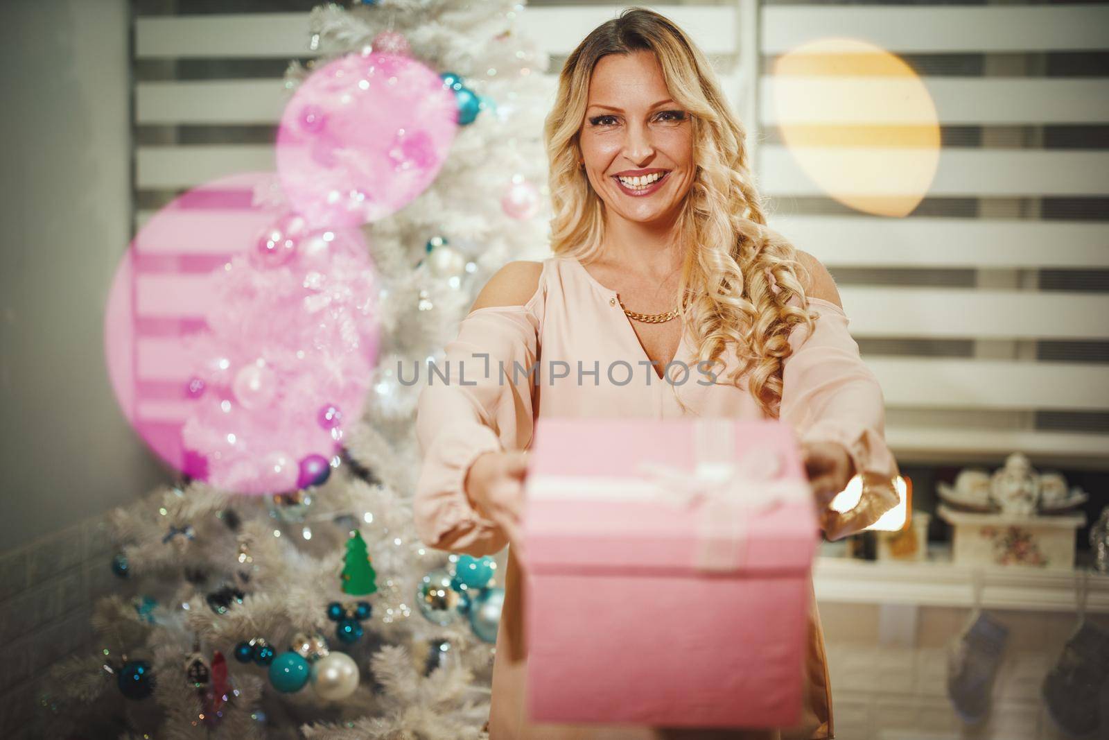 Shot of an attractive young woman handing Christmas gift to her daugter in front of the white Christmas tree at the home.