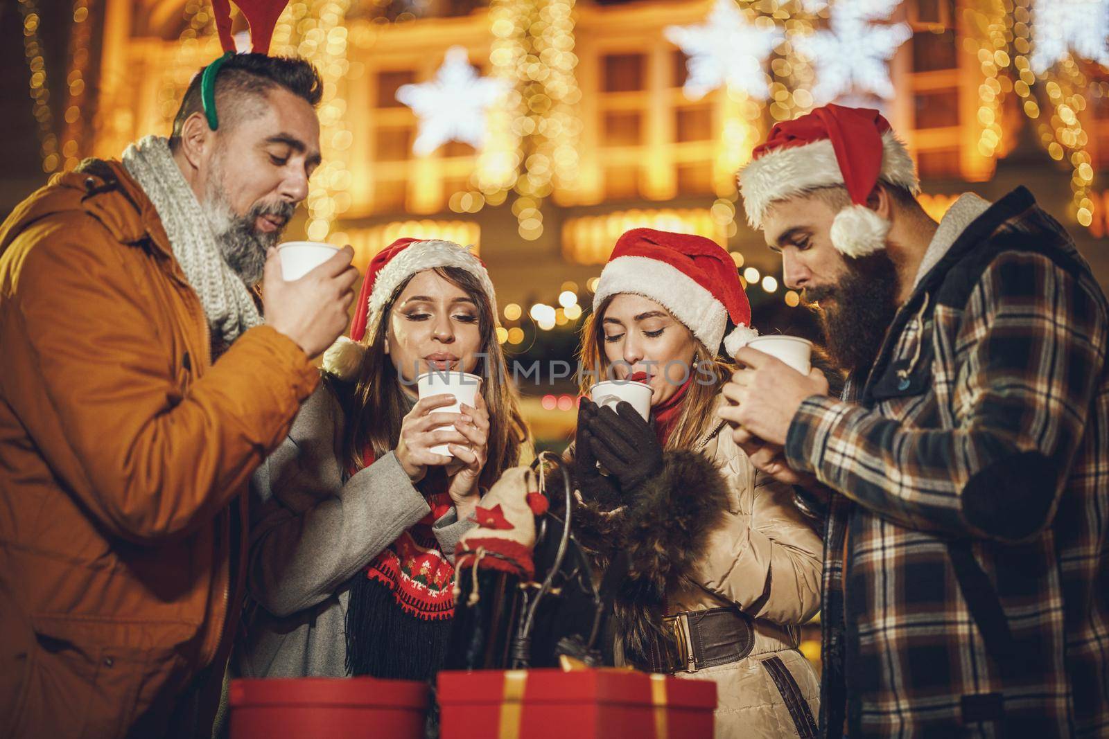 Shot of a group of cheerful young friends having fun together and enjoying mulled wine on the Christmas market at an evening party.
