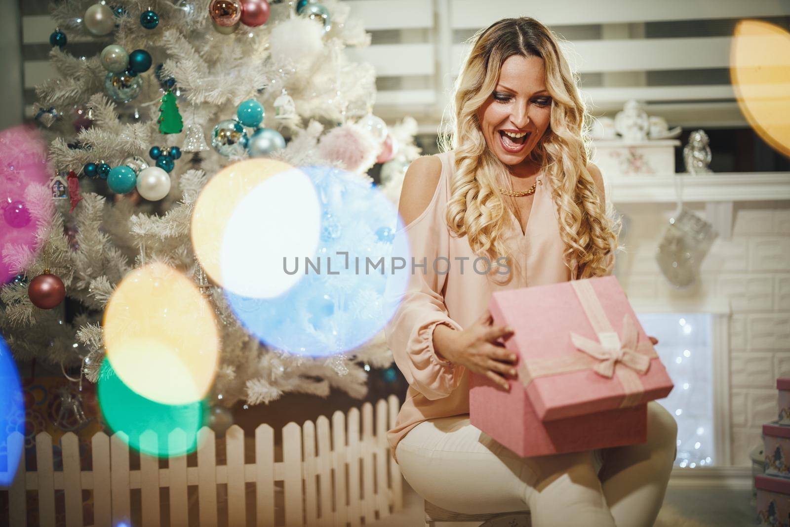 Shot of an attractive young woman opening her Christmas gift by a white Christmas tree at the home.