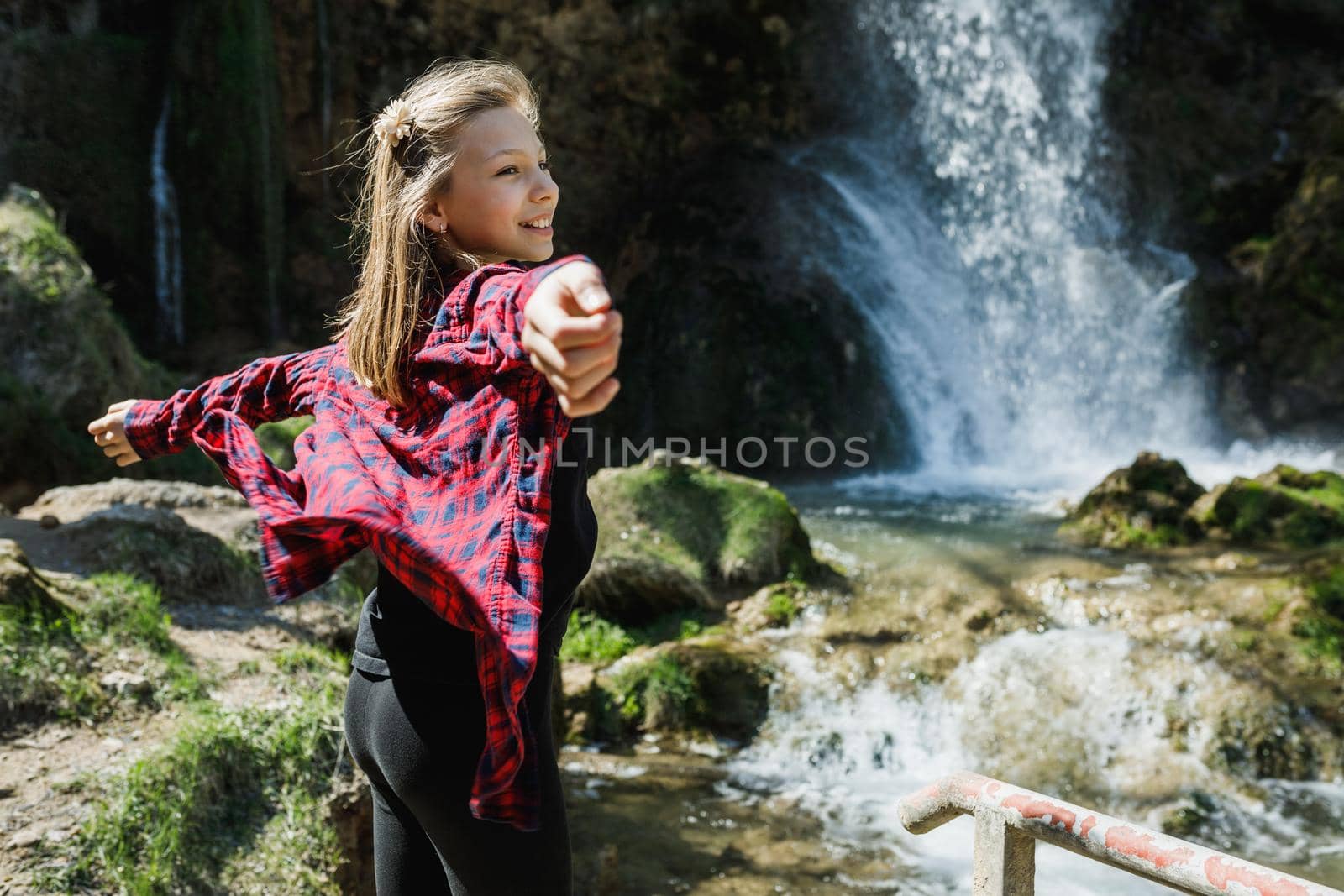 A smiling teenager girl enjoying the view of the beautiful waterfall.