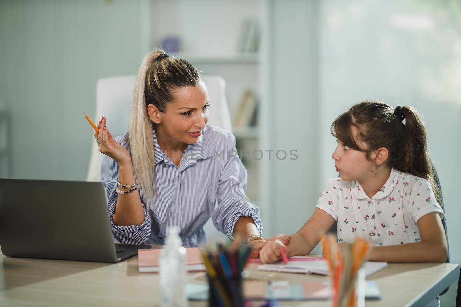 A beautiful young mother helping her cute daughter with homework at home.