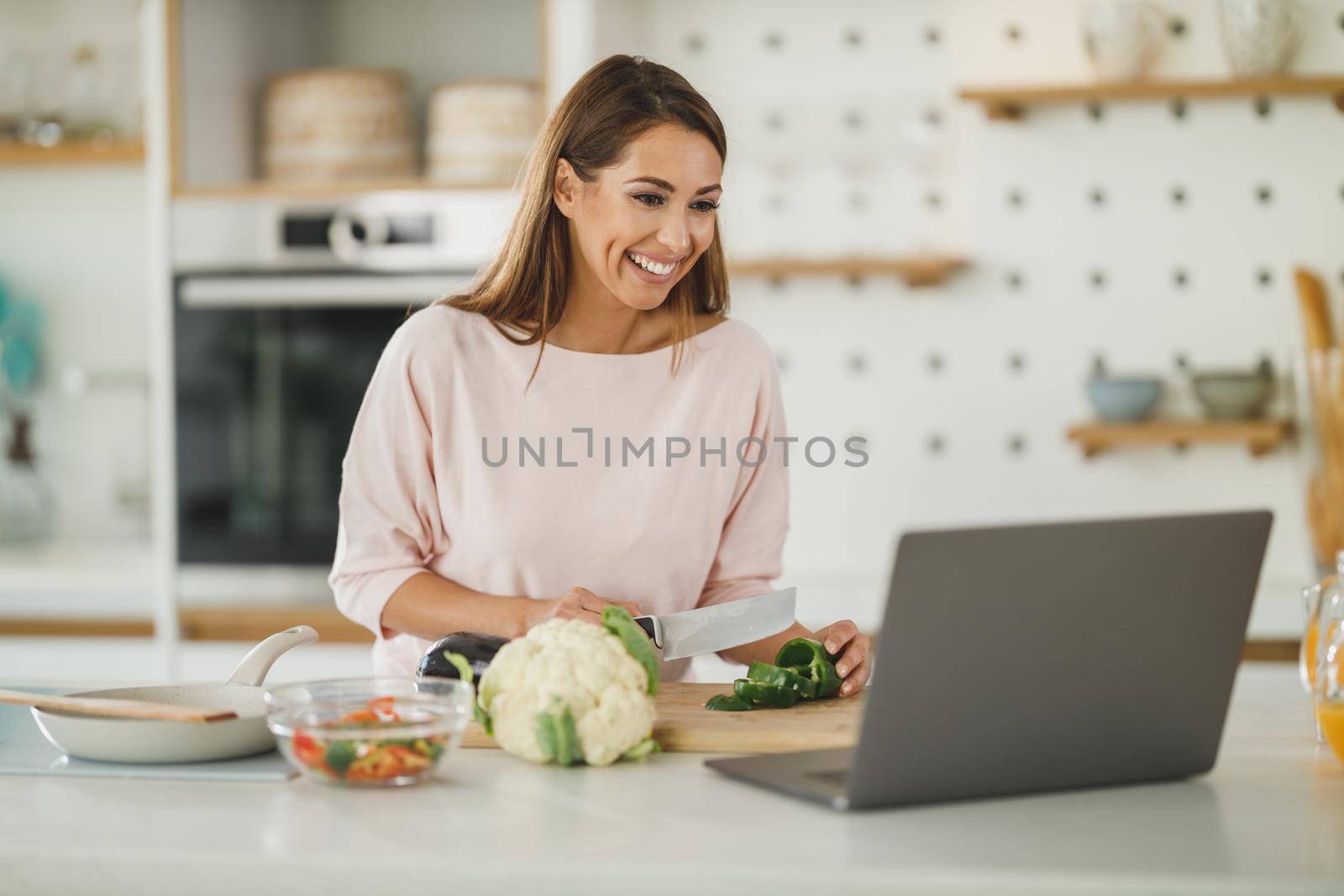 Shot of a young woman using a laptop while preparing a healthy meal at home.
