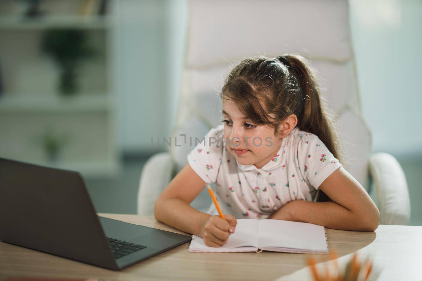 A cute diligent little girl using her laptop to do a online lesson at home.
